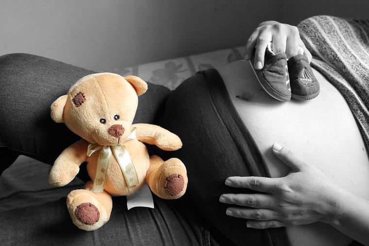 ventre nu de femme enceinte avec chaussons de bébé et nounours pour évoquer le congé maternité